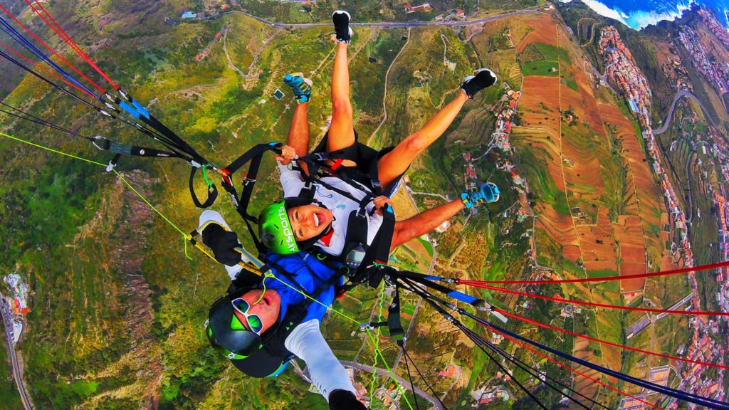 above perspective of tandem paragliders above green landscape